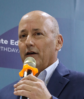 Headshot photo of Brad Ack holding microphone while speaking