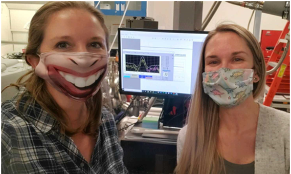 Two women wearing masks show a computer screen between them showing a graph