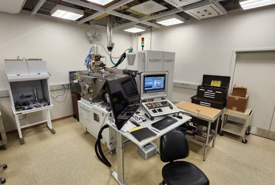 Laboratory space. A table with a computer and monitor sits in front of large machinery.